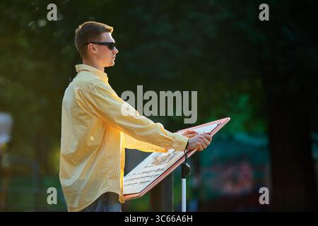 Side view of blind man reading outdoor tactile information board at sunset Stock Photo