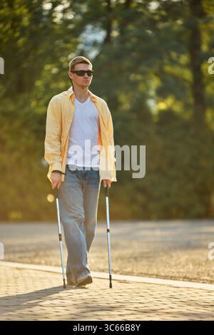 Blind man walking independently on park path using assistive trekking poles Stock Photo