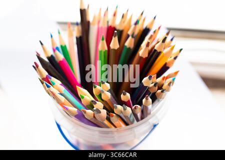 A bucket that is filled with various colored pencils resting on a table Stock Photo