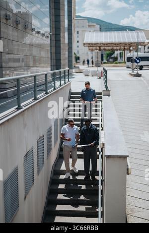 Three professionals discussing work documents while walking down outdoor stairs Stock Photo