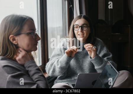 Two young women are collaborating on startup. Working with laptops, having discussion. Female business, working remotely, listen attentively Strategic Stock Photo