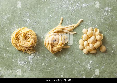 Variety of fresh raw uncooked homemade pasta. Spaghetti, tagliatelle and shells pasta on a floured work surface. Stock Photo