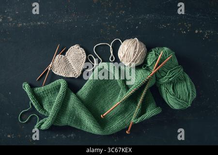 Knitting project with white and green wool and bamboo needles on rustic background. Incomplete knitting project with wooden needles. Stock Photo