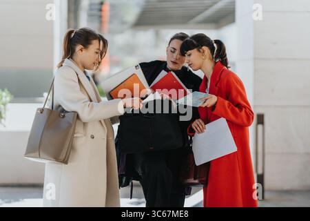 Three female professionals collaborating on a project outdoors while reviewing documents Stock Photo