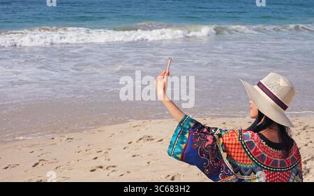 Woman in Colorful Outfit and Wide Brim Hat Enjoy Taking Selfies on the Wavy Seaside Stock Photo