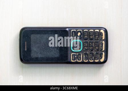 Top view of an old, used button-style mobile phone on a light wooden background. Stock Photo