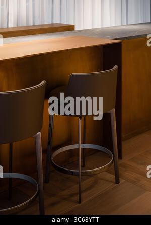 Couple of bar stools near high brass-bronze colored table. Empty high chairs in lobby lounge bar with warm lighting. Stock Photo