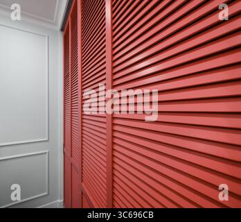 Red louver panel inside a white room. Perspective view of pale red hinged window shutters with horizontal stripes. Stock Photo
