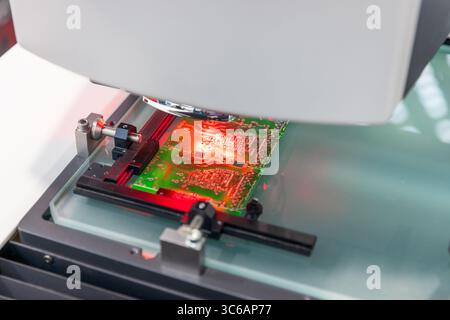 Close-up of an automated optical inspection (AOI) machine examining a printed circuit board (PCB) under red light during the electronics manufacturing Stock Photo