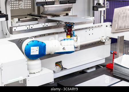 Close-up of collaborative robotic arm manipulating metal sheet in high-tech automated factory environment. Modern CNC press brake machinery, precision Stock Photo