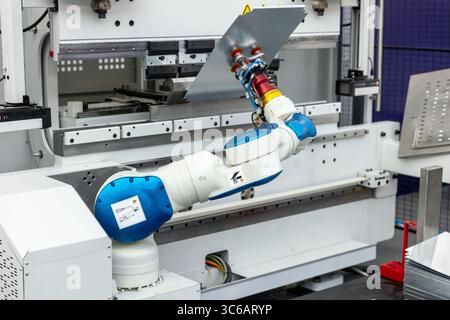Close-up of collaborative robotic arm manipulating metal sheet in high-tech automated factory environment. Modern CNC press brake machinery, precision Stock Photo