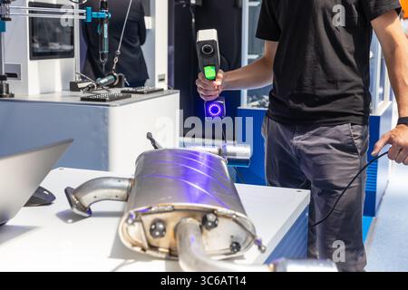 Close-up view of a technician using a handheld 3D laser scanner to scan an automotive exhaust component. The scanning process involves blue structured Stock Photo