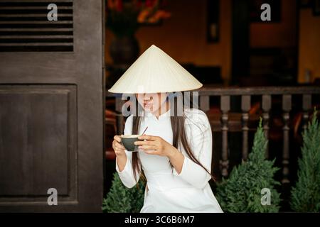 Vietnamese woman in ao dai drinking coffee, Hoi An, Quảng Nam Province, Vietnam Stock Photo