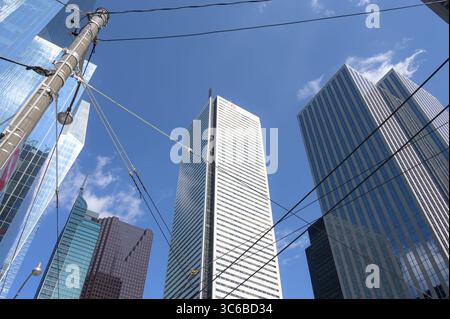 The white BMO Tower rises at the center of a cluster of downtown skyscrapers, framed by power lines and a bright blue sky. Stock Photo