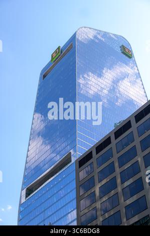 The curved glass facade of the TD Terrace tower reflects the sky and clouds above a modern office block. Stock Photo