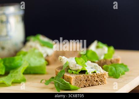 Slice of rye bread with cheese spread and greens on the table. Stock Photo