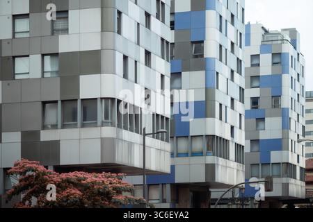 Contemporary residential buildings with a geometric checkerboard facade of blue, grey, and white panels, featuring cantilevered upper floors, city inf Stock Photo