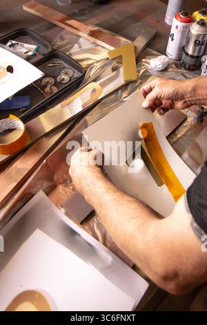Close-up of artist crafting gold number stencils with spray paint on a cluttered workshop table. Great for themes of creativity, DIY, and hands-on art. Stock Photo