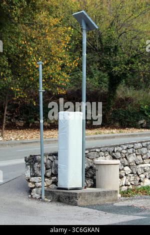 A solar-powered roadside speed camera stands beside a stone wall, temporarily wrapped for maintenance or installation, enhancing traffic safety Stock Photo