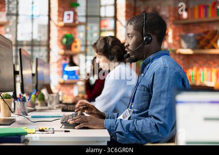 Multiethnic team of call center agents using remote access tools to connect to customer devices, fixing errors. Workers in diverse customer center workspace assisting clients with installing software Stock Photo