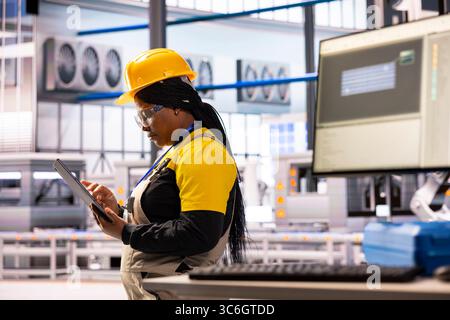 Smart factory consultant using her tablet, running a system performance check. African american female engineer with digital device working on technological advancement in manufacturing plant. Stock Photo