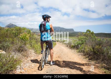 Mountain bike resting on dirt trail winding through rocky scrubland under flat-topped mountains. Adventure, exploration, outdoor, rugged, activity, na Stock Photo