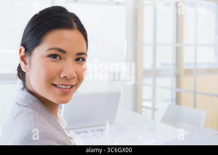 Asian woman sitting at table in office meeting room reviewing printed charts on laptop, copy space. Professional, corporate, workspace, modern, produc Stock Photo