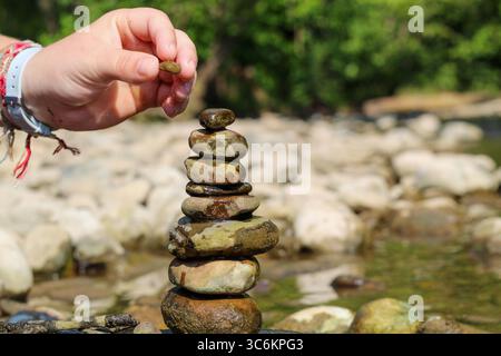 Close-Up of Hands Stacking Rocks by a Stream in a Peaceful Natural Environment Stock Photo