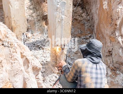 The worker is using an oxy-acetylene torch to cut reinforcement bars embedded in the concrete pile. Stock Photo