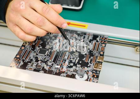 Technician working on a circuit board in a high-tech electronics lab during daytime Stock Photo