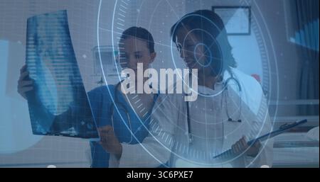 Two medics in scrubs holding X-ray film and reviewing clipboard in exam room with digital overlay Stock Photo