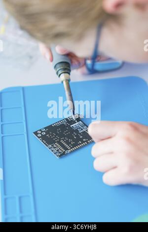 Person soldering on a circuit board lying on a blue base Stock Photo