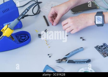 Working with electronic components on a table, soldering iron and hands clearly visible Stock Photo