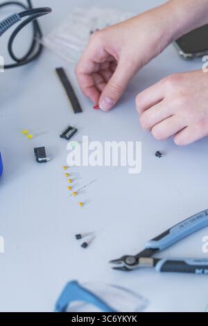 Hands working with small electronic components and tools on a table Stock Photo