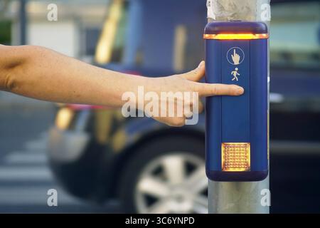 A man presses a pedestrian button on a traffic light with a car driving  in the background. Smart infrastructure encouraging safe navigation Stock Photo