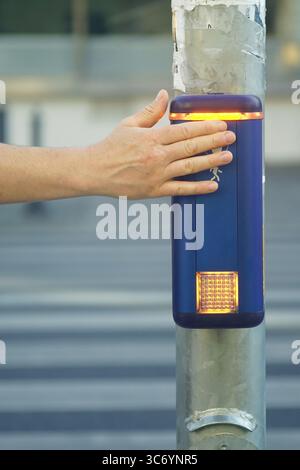 Close-up of hand pressing pedestrian crossing button with illuminated signal. City infrastructure element designed for traffic control, public safety Stock Photo