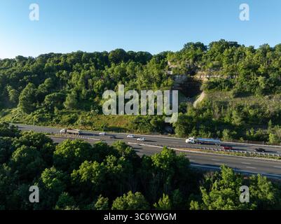 Multilane highway seen from above, side view on a sunny morning. Blurred traffic seen flowing in both directions, down a tree covered mountain. Stock Photo