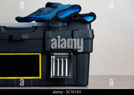 Close-up of blue protective work gloves resting on a black plastic toolbox with a yellow label. Perfect for themes of DIY and home repair Stock Photo