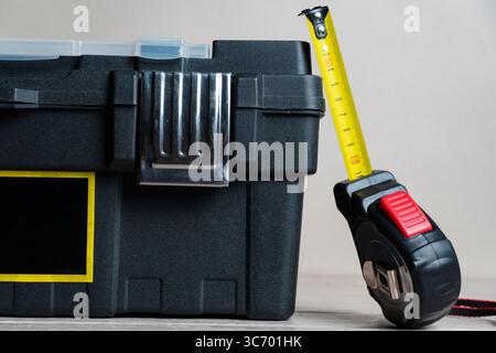 Black metal toolbox with an open lid and a yellow measuring tape extended beside it, isolated on a white background Stock Photo