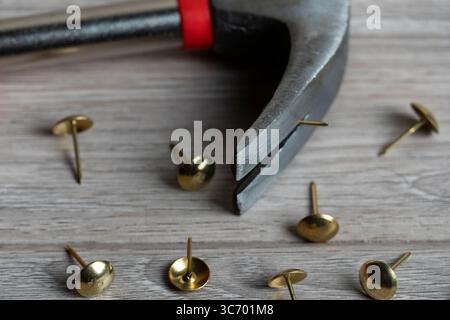 A close-up image of a hammer with a red grip and several brass tacks scattered on a wooden surface Stock Photo