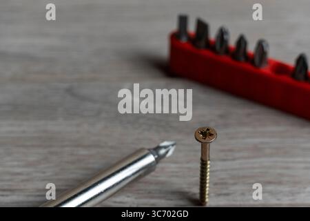 Close-up of a screwdriver and screw tip on a wooden workbench with a red tool bit set in the background Stock Photo