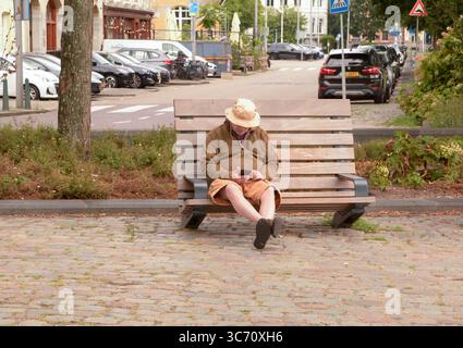 Man sat on a wooden seat checking his smartphone in Veerhaven, Rotterdam, The Netherlands Stock Photo