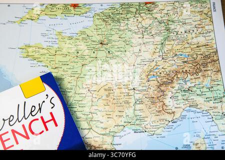 Open atlas focused on France alongside a "Travellers French" language guidebook, symbolizing travel planning and language learning. Stock Photo