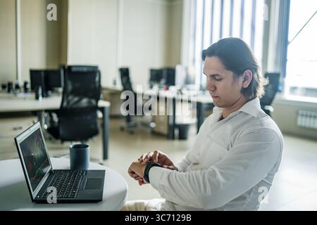 Man checks smart watch during coffee break at modern office. Stock Photo