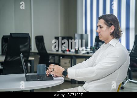 Man works on laptop with coffee in modern, bright office. Stock Photo