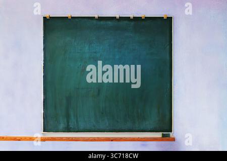 Empty green chalkboard on  a slightly worn purple wall inside an old classroom or studio. Vintage board with copy space Stock Photo