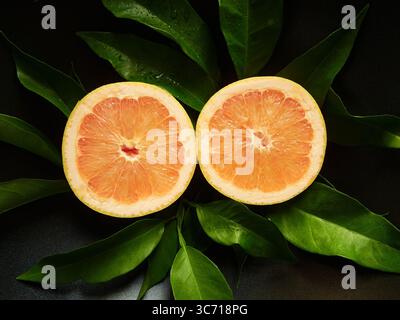 Halved Grapefruit on Green Leaves Displayed Against a Dark Background Stock Photo