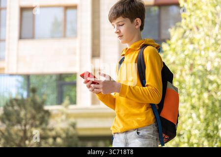 Preteen boy using smartphone outdoors, looking at screen, symbolizing digital childhood and modern technology use Stock Photo