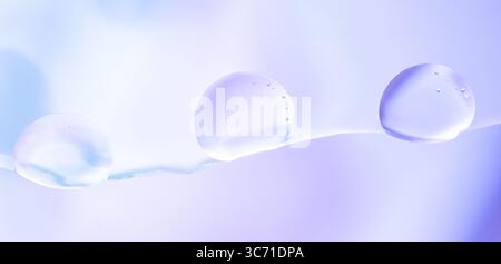 Macro shot of transparent liquid drops with subtle reflections on a cool blue and purple gradient background. Banner Stock Photo