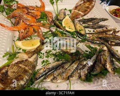 A delicious seafood platter with grilled fish, shrimp, and mussels on a white plate. Stock Photo